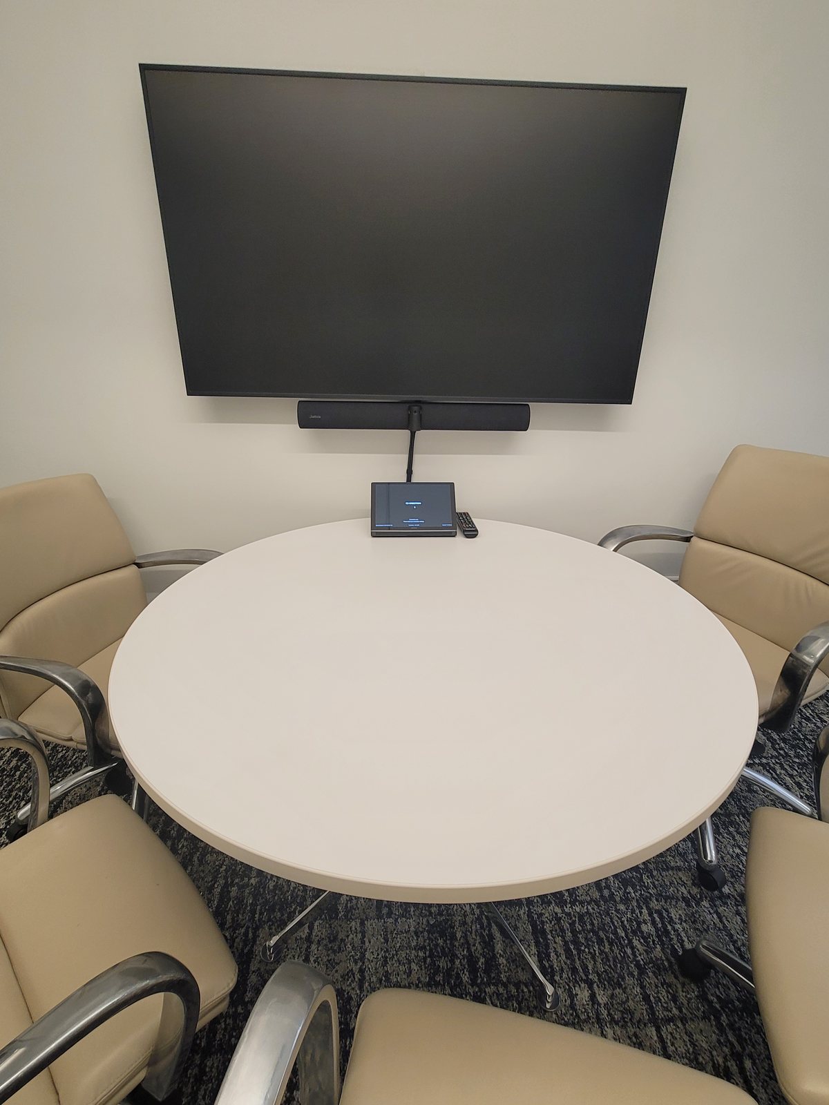 Small meeting room with a round table, wall display and video bar
