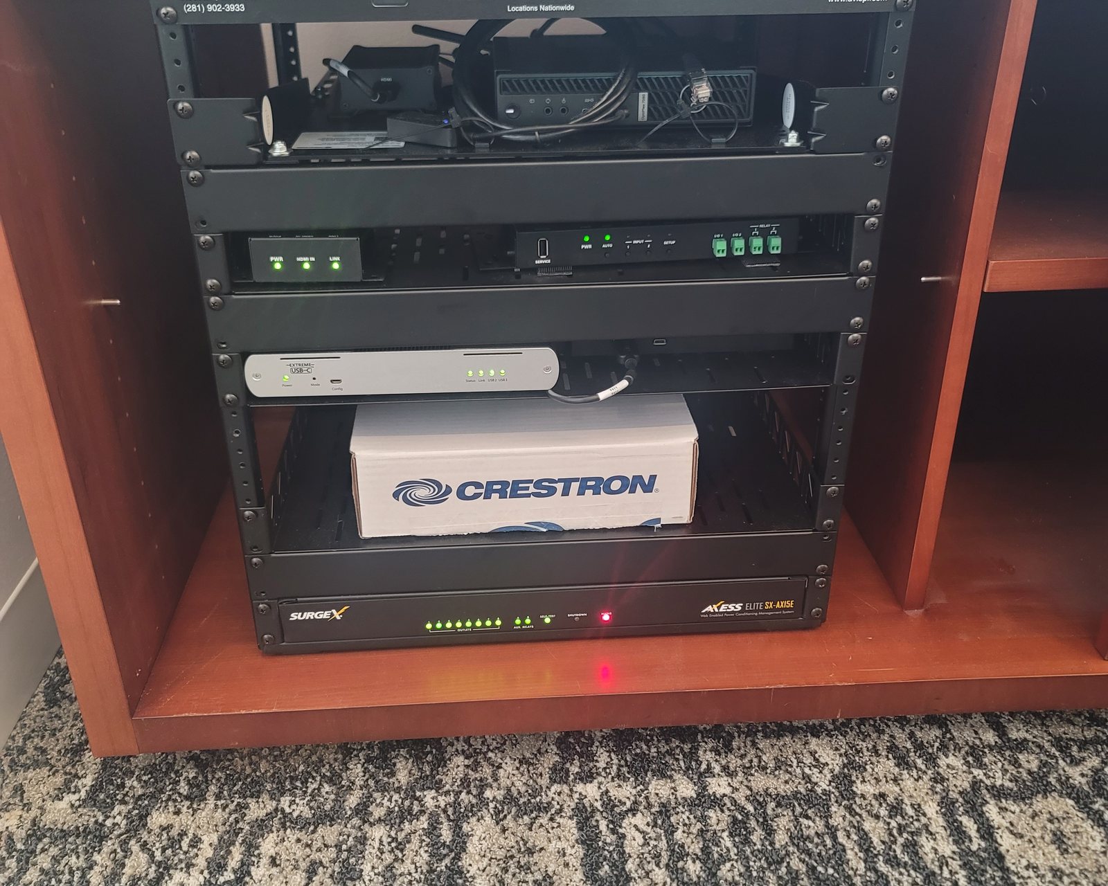 Equipment rack in a wood cabinet with Crestron-branded equipment on the lower shelf