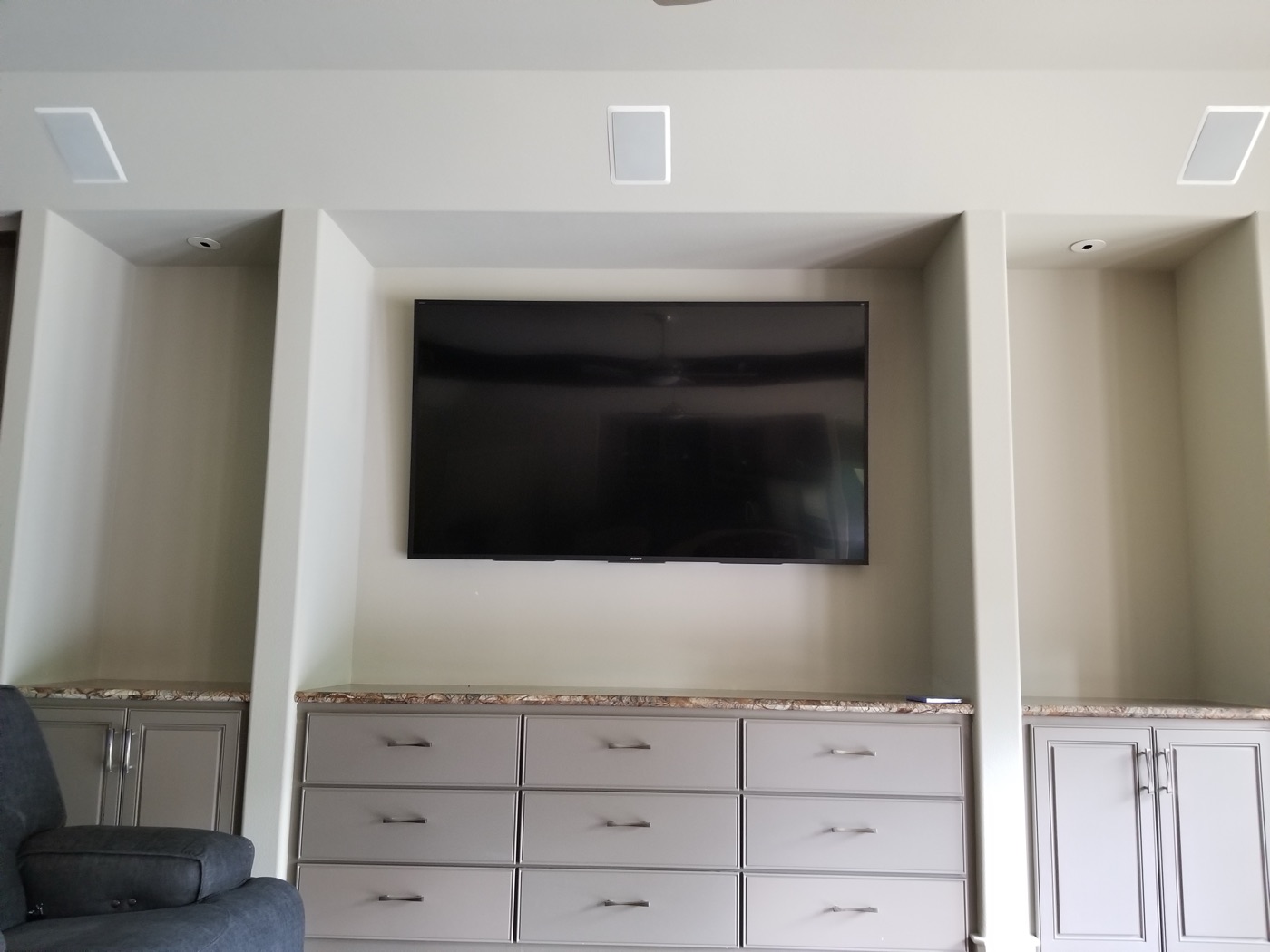 Wall-mounted TV in a built-in niche with three in-wall speakers above in a North Spring home
